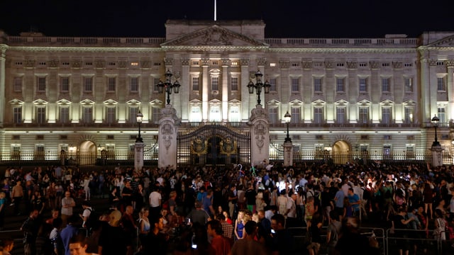 Beleuchteter Buckingham Palace am Abend, davor eine Menschenmasse. Beleuchteter Buckingham Palace am Abend, davor eine Menschenmasse.