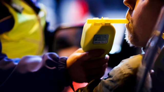 Polizist lässt Autofahrer in ein Alkoholmessgerät blasen. Polizist lässt Autofahrer in ein Alkoholmessgerät blasen.