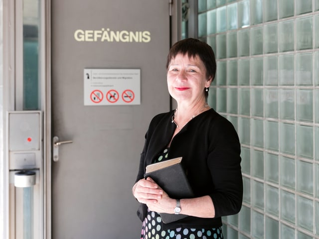 Eine Frau mit gepunktetem, farbigen Rock steht vor einer massiven Türe, welche die Aufschrift "Gefängnis" trägt. Eine Frau mit gepunktetem, farbigen Rock steht vor einer massiven Türe, welche die Aufschrift "Gefängnis" trägt.