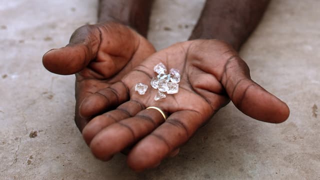 Symbolbild: Mehrere Rohdiamanten in der Handfläche eines Afrikanrs (es sind nur die Hände zu sehen).