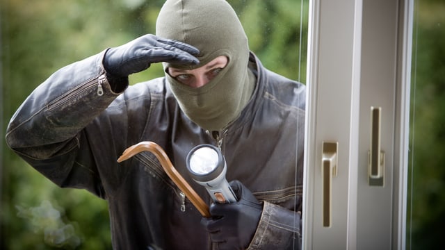 Ein Einbrecher mit Brecheisen schaut durch ein Fenster Ein Einbrecher mit Brecheisen schaut durch ein Fenster