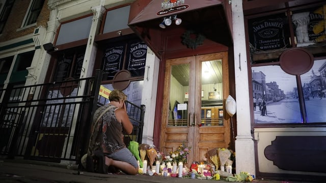 Frau kniet vor dem Eingang einer Bar. Am Boden viele Blumen und Gedenktafeln für die Toten. Frau kniet vor dem Eingang einer Bar. Am Boden viele Blumen und Gedenktafeln für die Toten.
