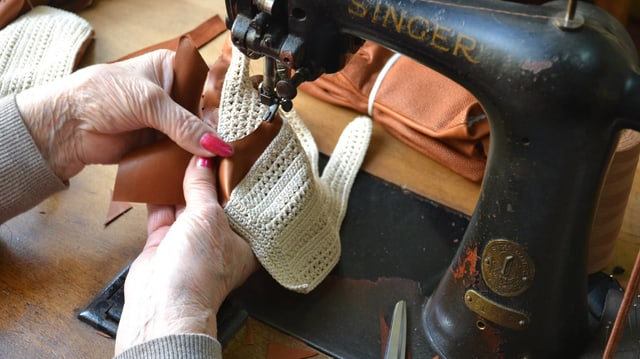 Eine Frau näht einen Handschuh an einer alten Singer-Nähmaschine. Eine Frau näht einen Handschuh an einer alten Singer-Nähmaschine.