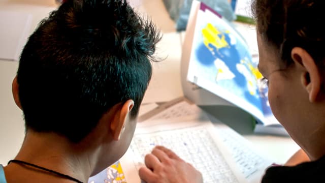 Ein Frau schaut mit einem Jungen ein Schulbuch an. Ein Frau schaut mit einem Jungen ein Schulbuch an.