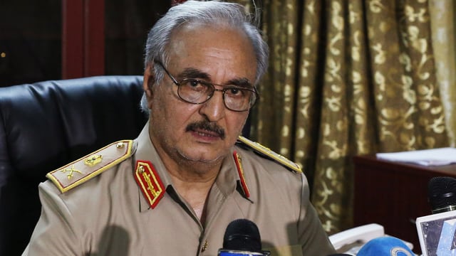 Haftar sitzt in seiner Generalsuniform vor mehreren Mikrofonen und blickt in die Kamera. Haftar sitzt in seiner Generalsuniform vor mehreren Mikrofonen und blickt in die Kamera.