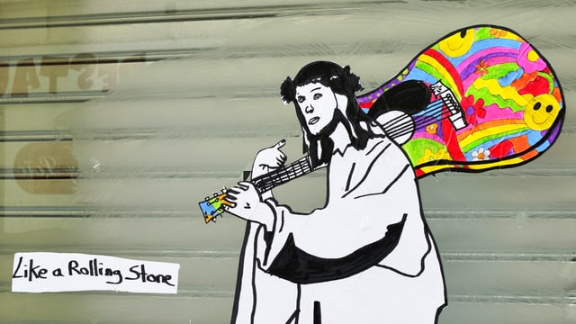 Strassenkunst: Jesus-Figur trägt bunte Gitarre über der Schulter. Strassenkunst: Jesus-Figur trägt bunte Gitarre über der Schulter.