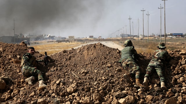 Kurdische Kämpfer liegen auf einem Erdwall, der eine Strasse blockiert.