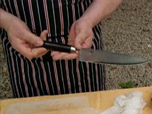 Ein Mann mit Kochschürze hält ein Kochmesser in seinen Händen.
