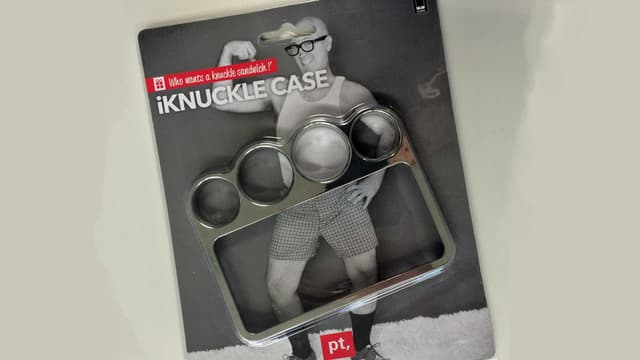 Handyhülle mit Schlagring in einer Verpackung mit einem untrainierten Mann, der in kurzen Hosen eine Pose macht. Handyhülle mit Schlagring in einer Verpackung mit einem untrainierten Mann, der in kurzen Hosen eine Pose macht.