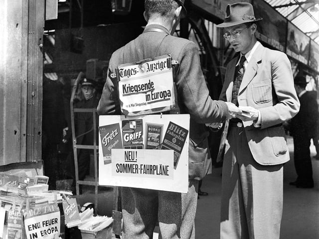 Ein Zeitungsverkäufer trägt Schilder mit den Schlagzeilen des Tages am 8. Mai 1945. Ein Zeitungsverkäufer trägt Schilder mit den Schlagzeilen des Tages am 8. Mai 1945.