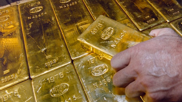 Ein Mann greift nach einem Goldbarren Ein Mann greift nach einem Goldbarren