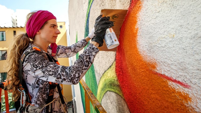 Eine Frau bemalt mit einer Sprühdose eine Wand. Eine Frau bemalt mit einer Sprühdose eine Wand.