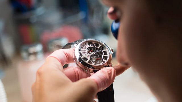 Uhrmacher von hinten fotografiert hält mit der linken Hand eine Uhr vor die Augen Uhrmacher von hinten fotografiert hält mit der linken Hand eine Uhr vor die Augen