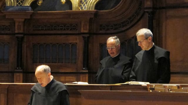 Drei Männer in Mönchskutten stehen singend hinter aufgeschlagenen Büchern. Drei Männer in Mönchskutten stehen singend hinter aufgeschlagenen Büchern.