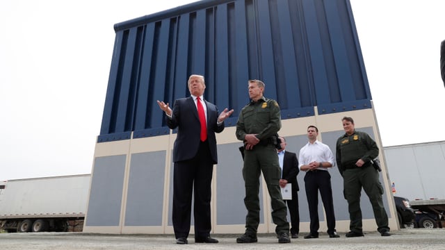 Trump mit Männern vor Mauerteil. Trump mit Männern vor Mauerteil.
