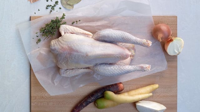 Ungekochtes Suppenhuhn mit gerüstetem Suppengemüse auf einem Schneidebrett. Ungekochtes Suppenhuhn mit gerüstetem Suppengemüse auf einem Schneidebrett.