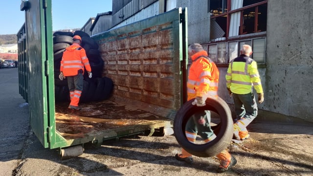 Arbeiter tragen Autoreifen in grosse Mulde. Arbeiter tragen Autoreifen in grosse Mulde.