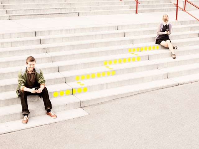 Ein Mann sitzt auf einer Treppe. Er schaut lächelnd in ein Smartphone. Eine gepunktete Linie führt von ihm weg die Treppe hinauf. Ein Mann sitzt auf einer Treppe. Er schaut lächelnd in ein Smartphone. Eine gepunktete Linie führt von ihm weg die Treppe hinauf.