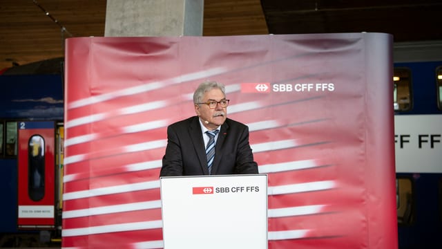 Toni Häne, grau meliert und in schwarzem Anzug, an einem Rednerpult, dahinter eine Stellwand der SBB. Toni Häne, grau meliert und in schwarzem Anzug, an einem Rednerpult, dahinter eine Stellwand der SBB.
