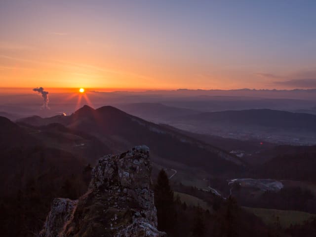 Orange Sonne am Horizont. Im Vordergrund Hügel noch im Schatten.