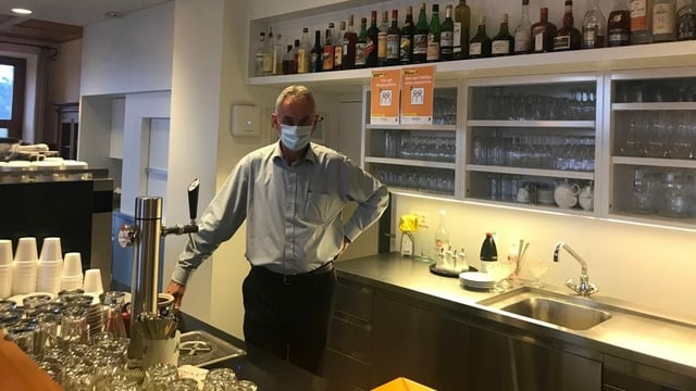 Primo Semadeni, in um grond e stigl cun chavels curts grischs ed ina mascra stà davos la bar da sia ustaria. Primo Semadeni, in um grond e stigl cun chavels curts grischs ed ina mascra stà davos la bar da sia ustaria.