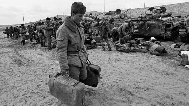 Ein russischer Soldat trägt seine Koffer. Im Hintergrund sind Panzer zu sehen. Ein russischer Soldat trägt seine Koffer. Im Hintergrund sind Panzer zu sehen.