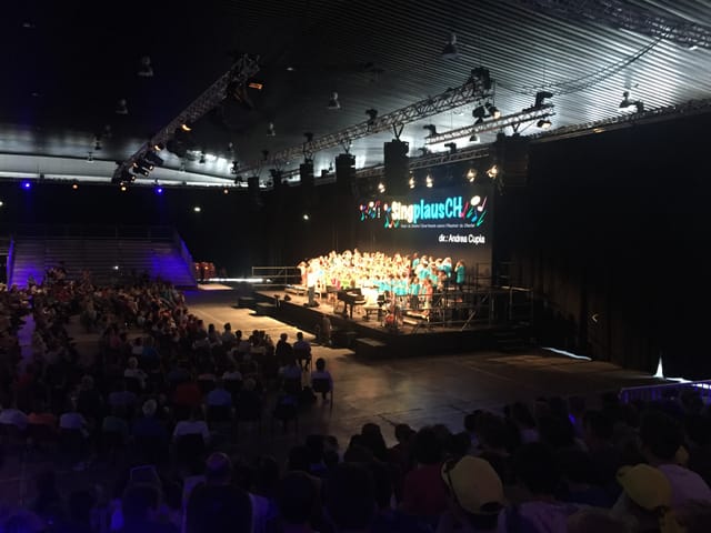 Purtret d'ina tribuna ed uffants che beneventan auters uffants.