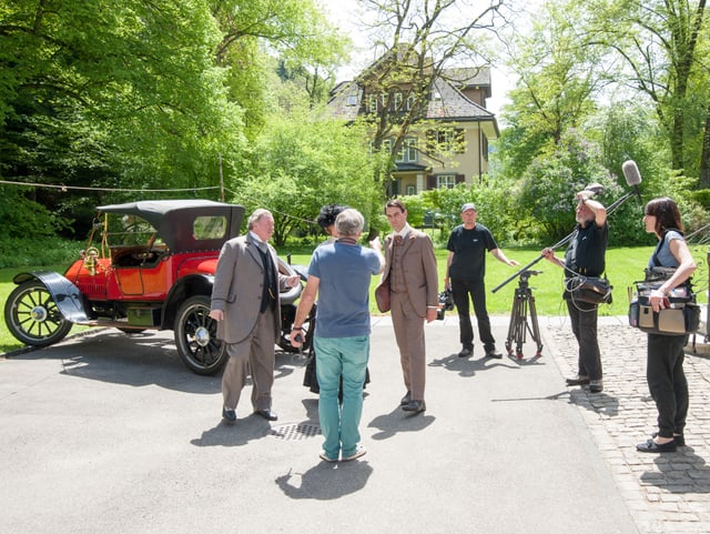 Fernsehteam und zwei Schauspieler draussen vor Villa, im Hintergrund Garland