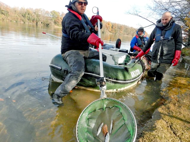 Drei Fischer stehen mit einem Fischernetz um ein grünes Gummiboot. Drei Fischer stehen mit einem Fischernetz um ein grünes Gummiboot.