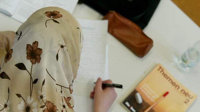 Mädchen mit Kopftuch an einem Schulpult sitzend Mädchen mit Kopftuch an einem Schulpult sitzend