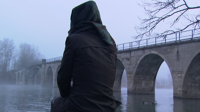 Eine Frau mit Kapuze sitzend an einem Fluss. Eine Frau mit Kapuze sitzend an einem Fluss.