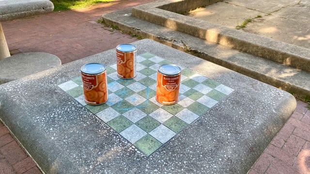 Auf einem Schachtisch hat jemand eine bescheidene Lebensmittel-Spende hinterlassen. Karottenbüchsen statt Schachfiguren. Auf einem Schachtisch hat jemand eine bescheidene Lebensmittel-Spende hinterlassen. Karottenbüchsen statt Schachfiguren.