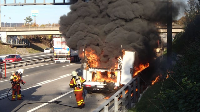 Feuerwehrleute hinter einem brennenden und stark rauchenden Lieferwagen Feuerwehrleute hinter einem brennenden und stark rauchenden Lieferwagen
