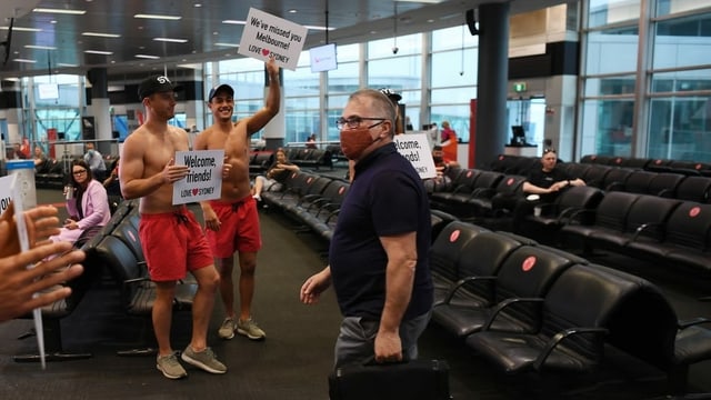 Passagier wird von Männern als Rettungsschwimmer verkleidet am Flughafen Sydney begrüsst. Passagier wird von Männern als Rettungsschwimmer verkleidet am Flughafen Sydney begrüsst.