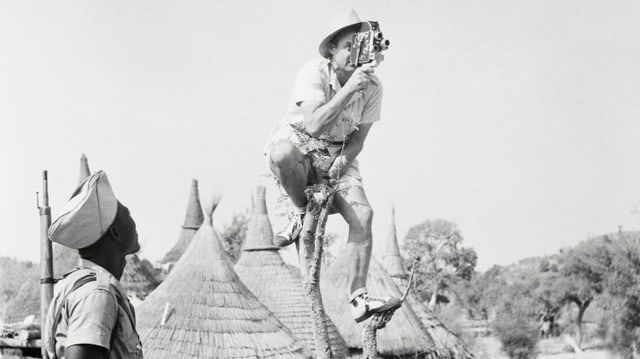 Ein Kameramann sitzt in Afrika auf einem dünnen Bäumchen, um von oben filmen zu können. Ein Kameramann sitzt in Afrika auf einem dünnen Bäumchen, um von oben filmen zu können.