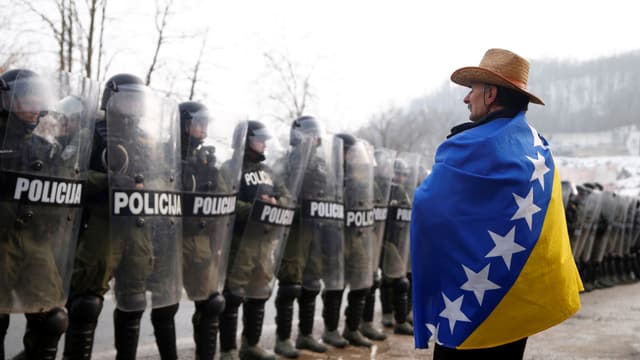 Eingehüllt in die Flagge Bosnien-Herzegovinas steht ein demonstrierender Veteran der Übermacht der Polizei gegenüber. Eingehüllt in die Flagge Bosnien-Herzegovinas steht ein demonstrierender Veteran der Übermacht der Polizei gegenüber.
