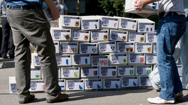 Zwei Männer biegen Kartonschachteln mit Unterschriften auf einem bereits gestapelten Kartonschachtel-Turm. Zwei Männer biegen Kartonschachteln mit Unterschriften auf einem bereits gestapelten Kartonschachtel-Turm.