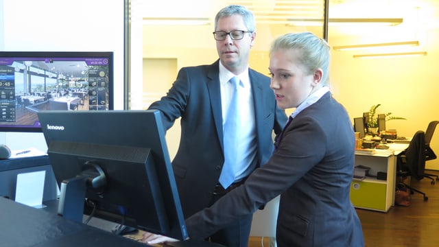 Mann und Frau in Anzug stehen vor Computer Mann und Frau in Anzug stehen vor Computer