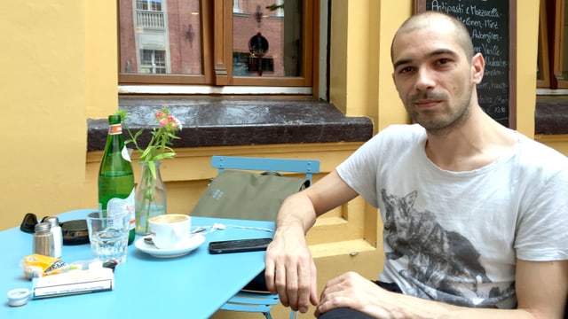 Bafis sitzt in einem Café, vor sich auf dem Tisch ein Handy und eine Tasse Kaffee. Bafis sitzt in einem Café, vor sich auf dem Tisch ein Handy und eine Tasse Kaffee.