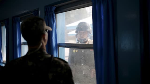 Nordkoreanischer Soldat blickt durch ein Fenster auf einen südkoreanischen Soldaten. Nordkoreanischer Soldat blickt durch ein Fenster auf einen südkoreanischen Soldaten.