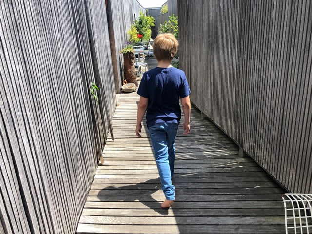 Ein Junge läuft barfuss auf einem Holzsteg. Der Schatten ist sehr kurz. Ein Junge läuft barfuss auf einem Holzsteg. Der Schatten ist sehr kurz.
