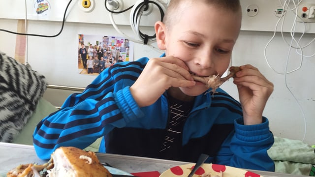 Mattia ist im Spitalbett und isst ein Poulet Mattia ist im Spitalbett und isst ein Poulet