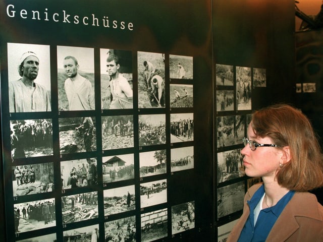 Eine Frau betrachtet Fotos in einer KZ-Ausstellung. Die Tafel heisst "Genickschüsse" Eine Frau betrachtet Fotos in einer KZ-Ausstellung. Die Tafel heisst "Genickschüsse"