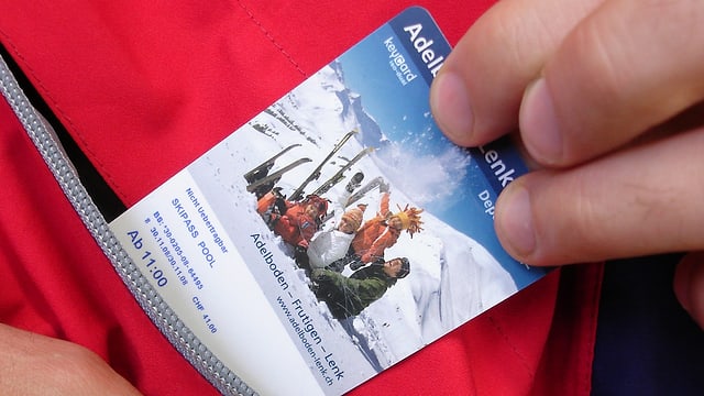 Eine Hand zieht eine Ski-Tageskarte aus einer Jackentasche. Eine Hand zieht eine Ski-Tageskarte aus einer Jackentasche.