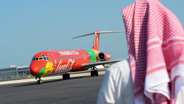 Fifa-Flugzeug im Hintergrund, dafür ein arabisch gekleideter Mann mit dem Rücken zur Kamera Fifa-Flugzeug im Hintergrund, dafür ein arabisch gekleideter Mann mit dem Rücken zur Kamera