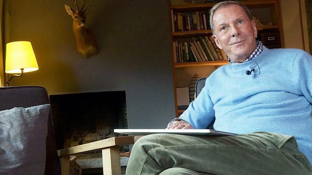 Ein älterer Mann sitzt im hellblauen Pulli und mit einem Buch in einem Sessel. Ein älterer Mann sitzt im hellblauen Pulli und mit einem Buch in einem Sessel.