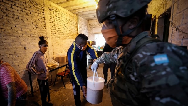 Soldat mit Gesichtsmaske, reicht Mann einen Eimer mit Essen. Soldat mit Gesichtsmaske, reicht Mann einen Eimer mit Essen.