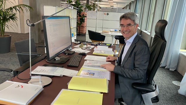 Purtret da Mario Cavigelli davos ses pult en biro Purtret da Mario Cavigelli davos ses pult en biro