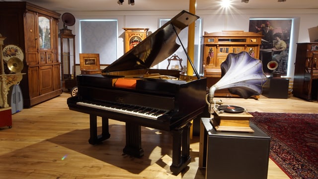 Ein Flügel. Daneben steht ein Phonograph mit einem Trichter, der einem Enzian gleicht. Ein Flügel. Daneben steht ein Phonograph mit einem Trichter, der einem Enzian gleicht.