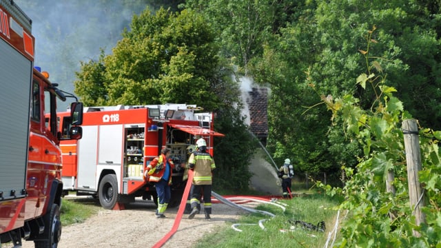 Zwei Feuerwehrautos und vier Feuerwehr-Einsatzkräfte bei der Arbeit. Zwei Feuerwehrautos und vier Feuerwehr-Einsatzkräfte bei der Arbeit.